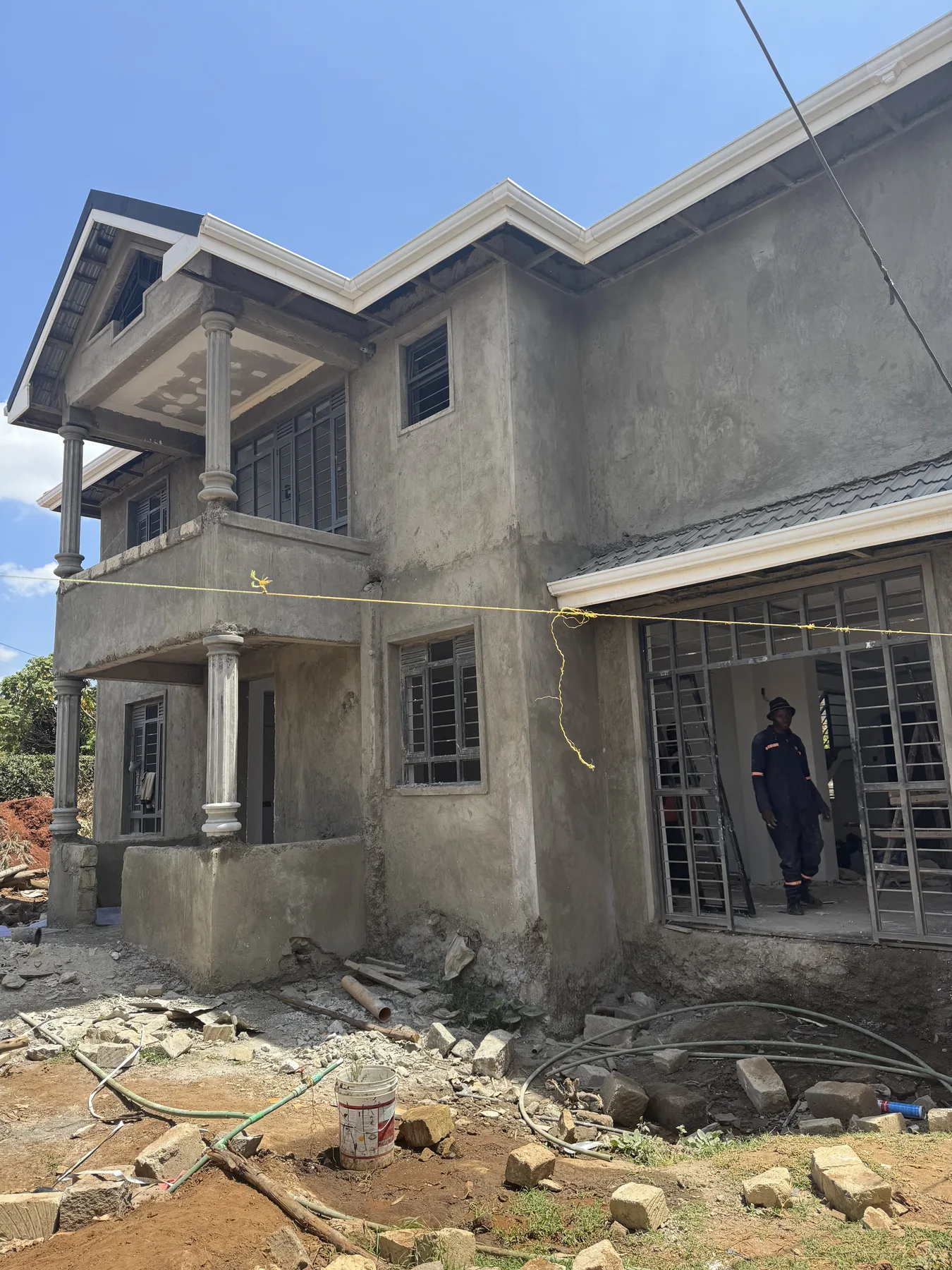Construction site: a two-storey house with plastered walls, columns and a balcony, workers at the entrance