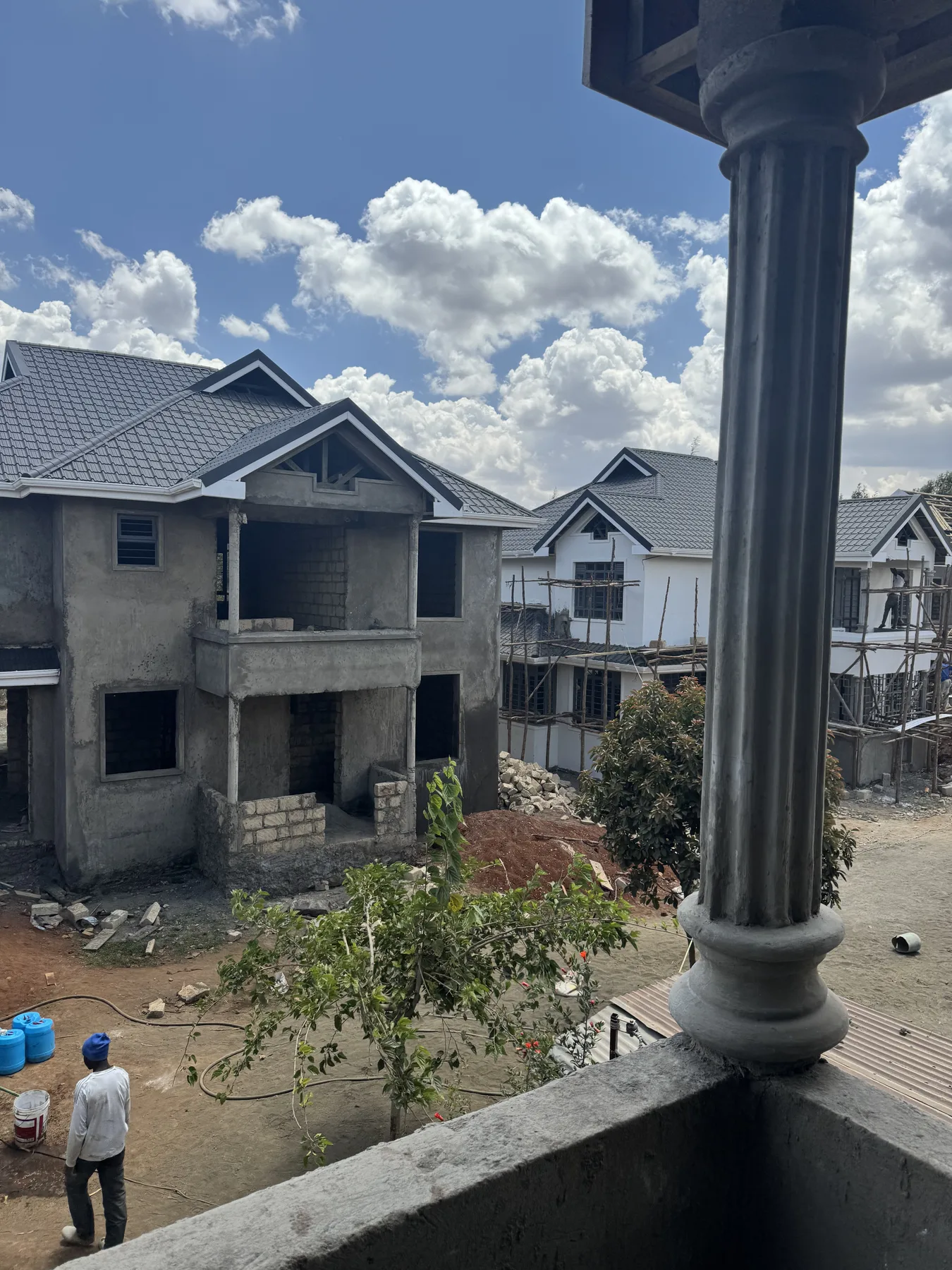 Construction site: a two-storey house shell with its roof on, seen from a neighbouring balcony